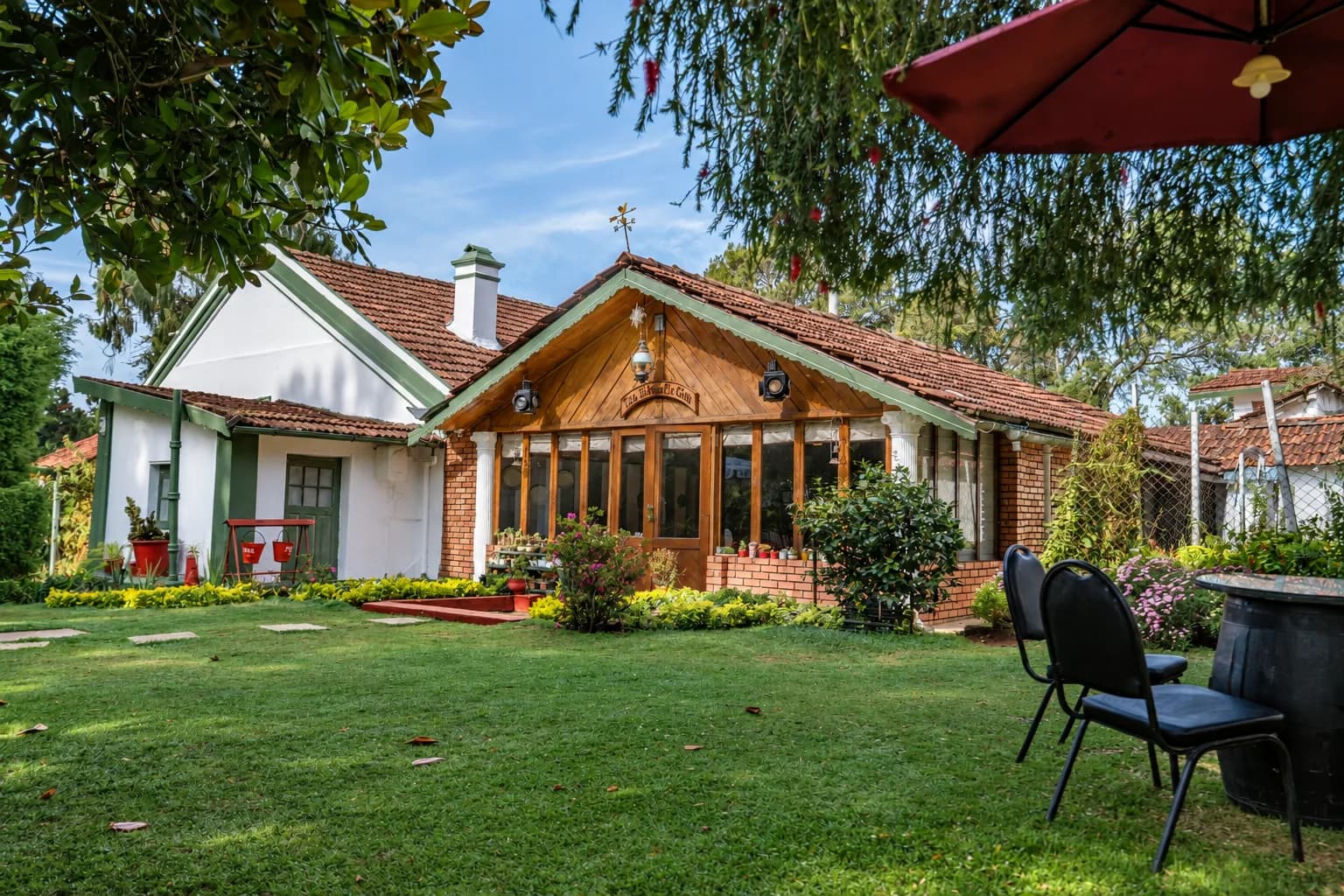 A red parasol and chairs on the lawn, the house behind